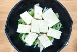 Firm tofu placed on onions in pan
