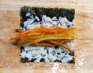 placing carrot fish cake and pickled radish fillings on rice for mini kimbap