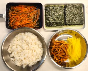 mini kimbap ingredients including rice seaweed carrot fish cake and pickled radish